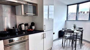 A modern kitchen with stainless steel appliances, a dining area with a table and chairs, and a view of the city through large windows. - Modern 2-Bed Flat in York City Centre - Steps from Minster and Shambles (York)