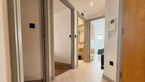 A hallway with wooden flooring and white walls, leading to a bathroom with a sink and a shower area. - Modern 2-Bed Flat in York City Centre - Steps from Minster and Shambles (York)