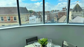 A dining area with a table set for two, a potted plant, and a view of the cityscape through large windows. - Modern 2-Bed Flat in York City Centre - Steps from Minster and Shambles (York)