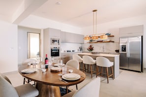A modern kitchen with a central island, stainless steel appliances, and a dining area with a round table set for four. - Brand New Ocean View Condo with Infinity Pool (Playa Tamarindo)
