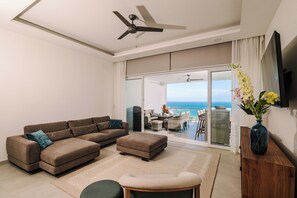 A modern living room with a sectional sofa, a small round table, and a view of the ocean through large sliding doors. - Brand New Ocean View Condo with Infinity Pool (Playa Tamarindo)