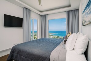 A hotel room with a large bed, a flat-screen TV, and a view of the ocean. - Brand New Ocean View Condo with Infinity Pool (Playa Tamarindo)