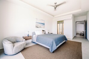 A bedroom with a bed, a chair, a nightstand, a painting, and a ceiling fan.