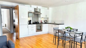 Una cocina moderna con armarios blancos, electrodomésticos de acero inoxidable y un comedor con mesa y sillas.