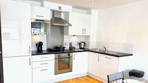Una cocina moderna con armarios blancos, electrodomésticos de acero inoxidable, horno empotrado y encimera negra.