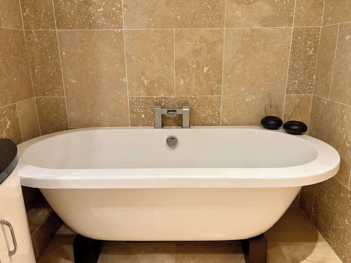 Uma banheira padrão em um banheiro com azulejos bege nas paredes.