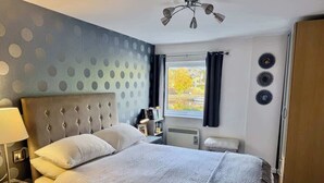 Habitación de hotel con una cama grande, una mesita de noche con lámpara, una ventana con cortinas y un radiador.
