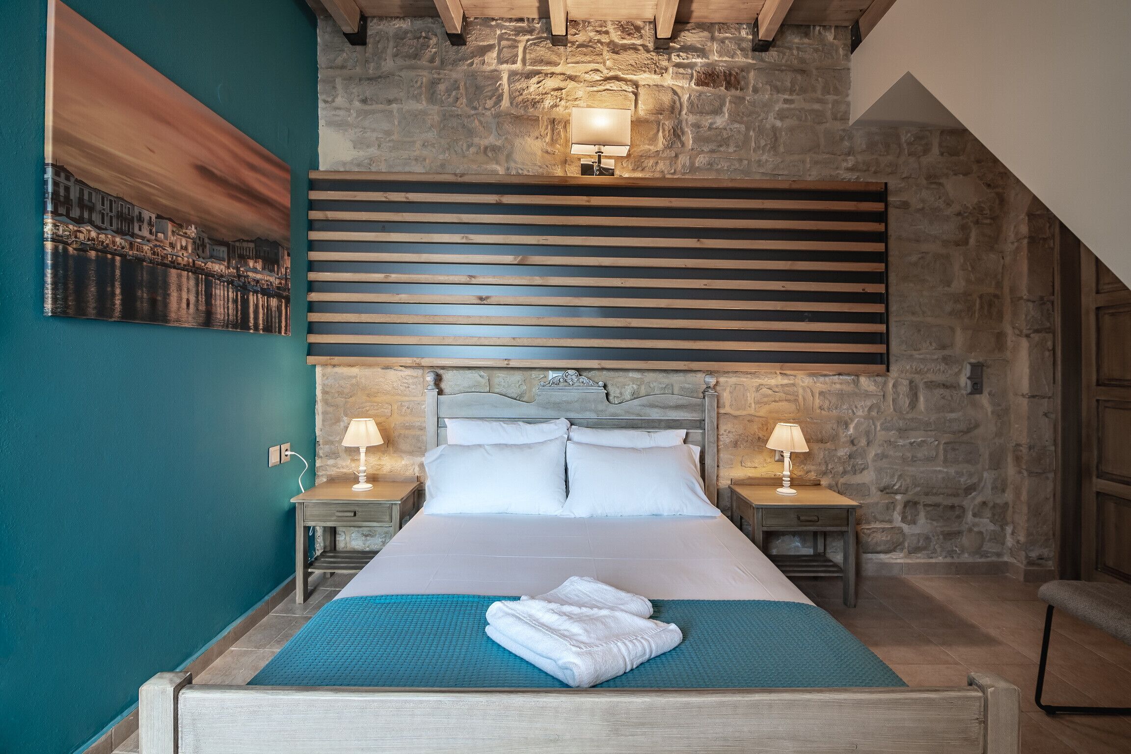 Een slaapkamer met een groot bed, stenen muren, een houten hoofdbord en twee nachtkastjes met lampen.