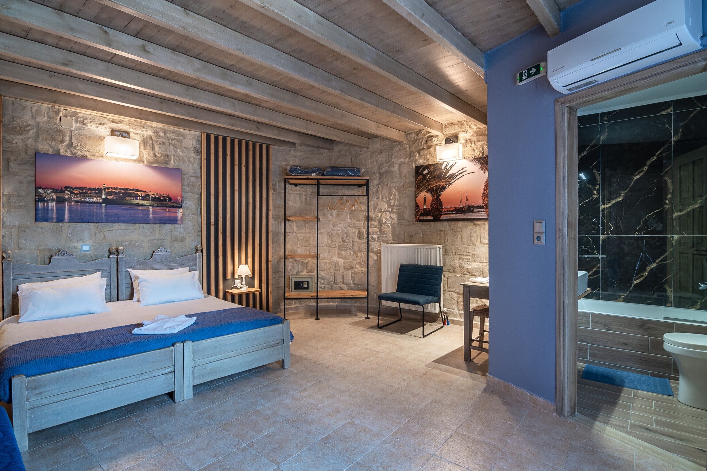 Een slaapkamer met een bed, een stoel, een nachtkastje, een wandplank en een schilderij.