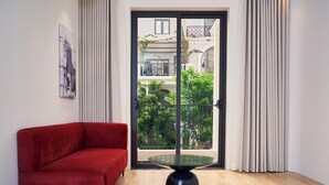 Een moderne woonkamer met een rode bank, een salontafel met glazen blad en uitzicht op een balkon met planten en een gebouw op de achtergrond.
