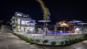 A modern outdoor pool area with lounge chairs and umbrellas, surrounded by a low wall and small plants. - Destino Apartments (Rethymno)