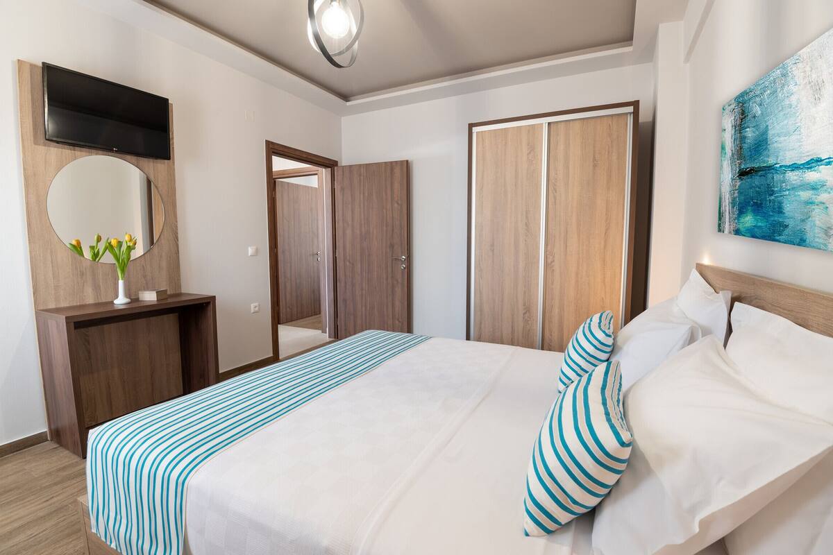 A hotel room with a bed, a TV mounted on the wall, a mirror, and a painting.