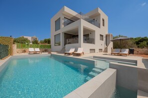 A modern two-story house with a swimming pool, lounge chairs, and a patio area. - Serenity Villa (Chania)