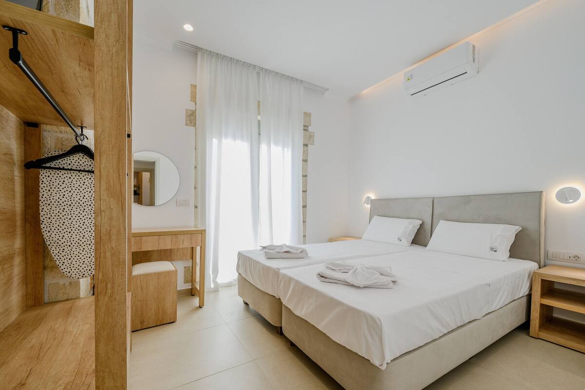 Una camera da letto con un letto, comodini, una scrivania in legno, uno specchio e un appendiabiti.