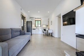 Un appartement moderne avec un canapé gris, un coin repas et une cuisine en arrière-plan.