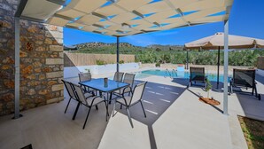 A patio with a pool, outdoor seating, and a stone wall. - Melidoni Villas (Mylopotamos)