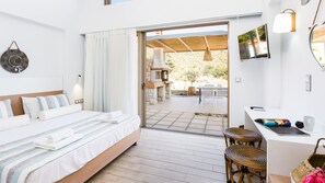 A modern hotel room with a bed, a desk, and a view of the outdoor patio. - Lemoni Villa (Mylopotamos)