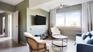 A modern living room with a flat-screen TV, a sofa, a chair, and a small table.