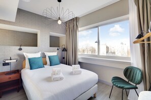 Ein modernes Hotelzimmer mit einem großen Bett, Blick auf die Stadt und einem grünen Sessel.