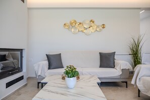 A modern living room with a white sofa, a marble coffee table, and a decorative wall piece. - Aether Group Villas (Rethymno)