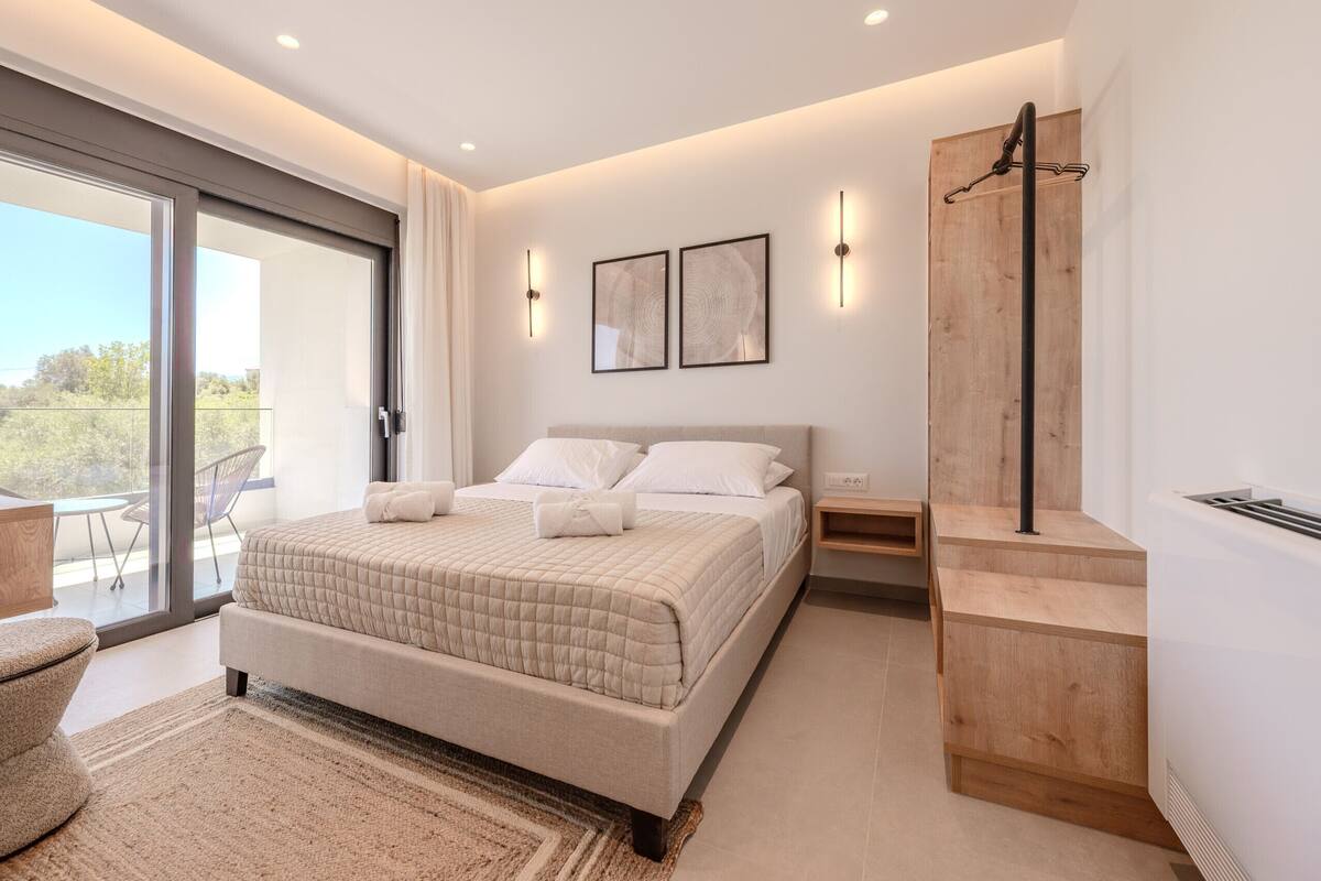 A modern bedroom with a large bed, a wooden side table, a built-in wardrobe, and a sliding glass door leading to a balcony.