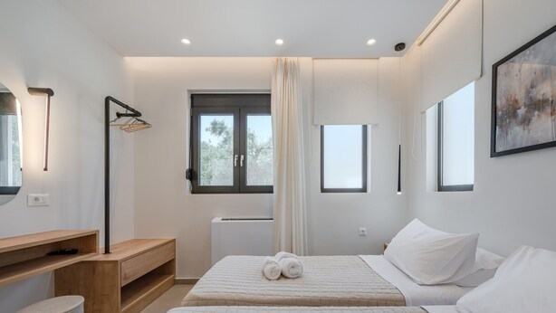 Une chambre moderne avec deux lits, un bureau en bois, une chaise et une grande fenêtre.