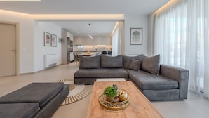 Un salon moderne avec un canapé d’angle gris, une table basse en bois et une cuisine en arrière-plan.
