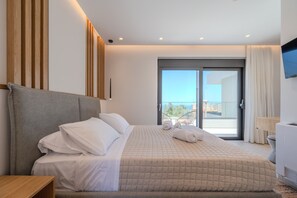 A modern hotel room with a large bed, a flat-screen TV, and a balcony with a view. - Aether Group Villas (Rethymno)