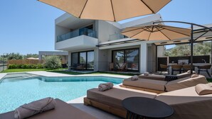 Un espace piscine extérieur moderne, doté de chaises longues et de parasols, d’un barbecue et d’un balcon fermé par des baies vitrées.