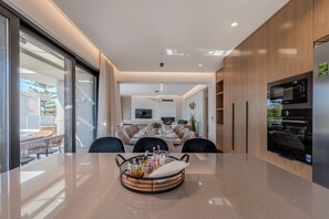 A modern kitchen with a large island, built-in appliances, and a dining area with a glass wall. - Aether Group Villas (Rethymno)