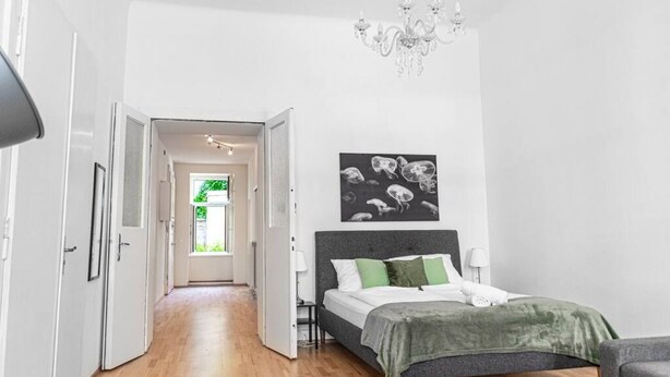 A bedroom with a bed, a chandelier, a hallway, and a door leading outside. - Modern 2BR Apt. Perfect for Long and Short Stays (Wien)
