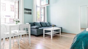 A room with a grey sofa, white chairs, a small table, and a window with a cityscape view. - Modern 2BR Apt. Perfect for Long and Short Stays (Wien)