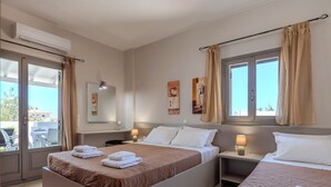 A hotel room with a large bed, a smaller bed, a desk with a lamp, a chair, and a window with curtains. - Aloe (Rethymno)