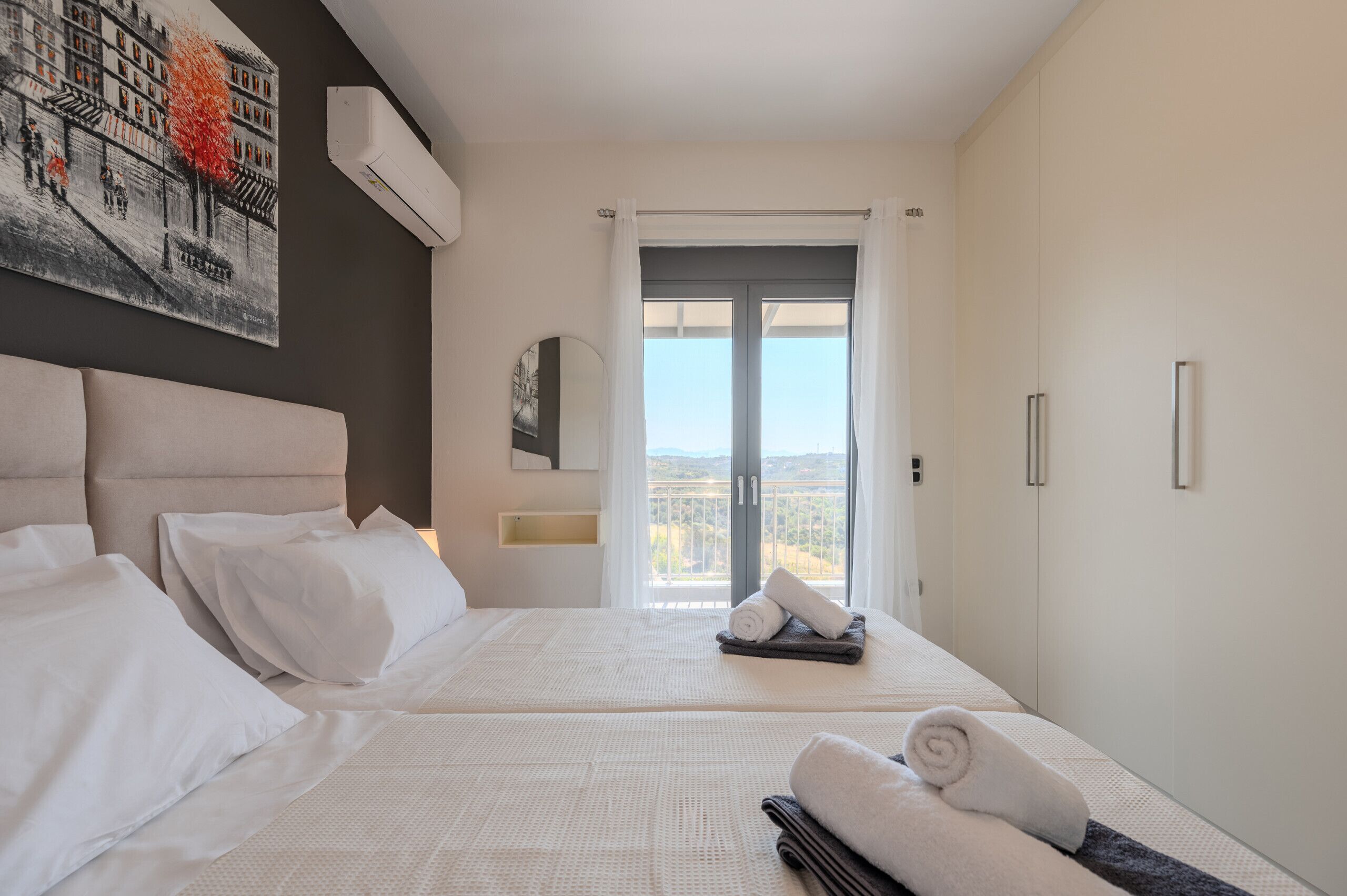 A hotel room with a large bed, a view of the city, and a painting on the wall.