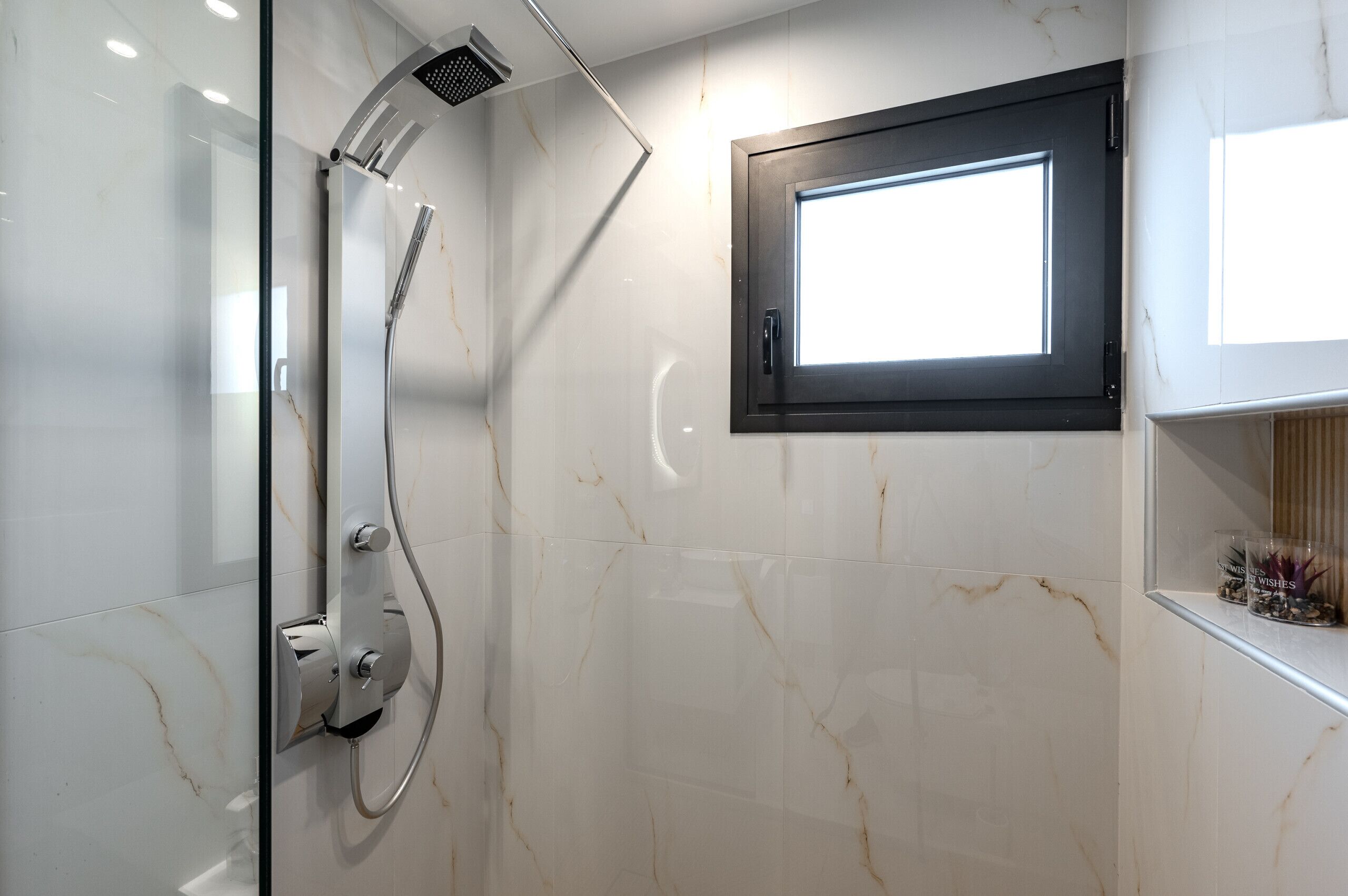 Een moderne badkamer met een douchecabine van glas, een inbouwraam en marmeren wanden.
