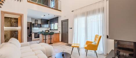 Una sala de estar moderna con un sofá, dos sillones, una mesa de centro, una chimenea y una cocina al fondo.