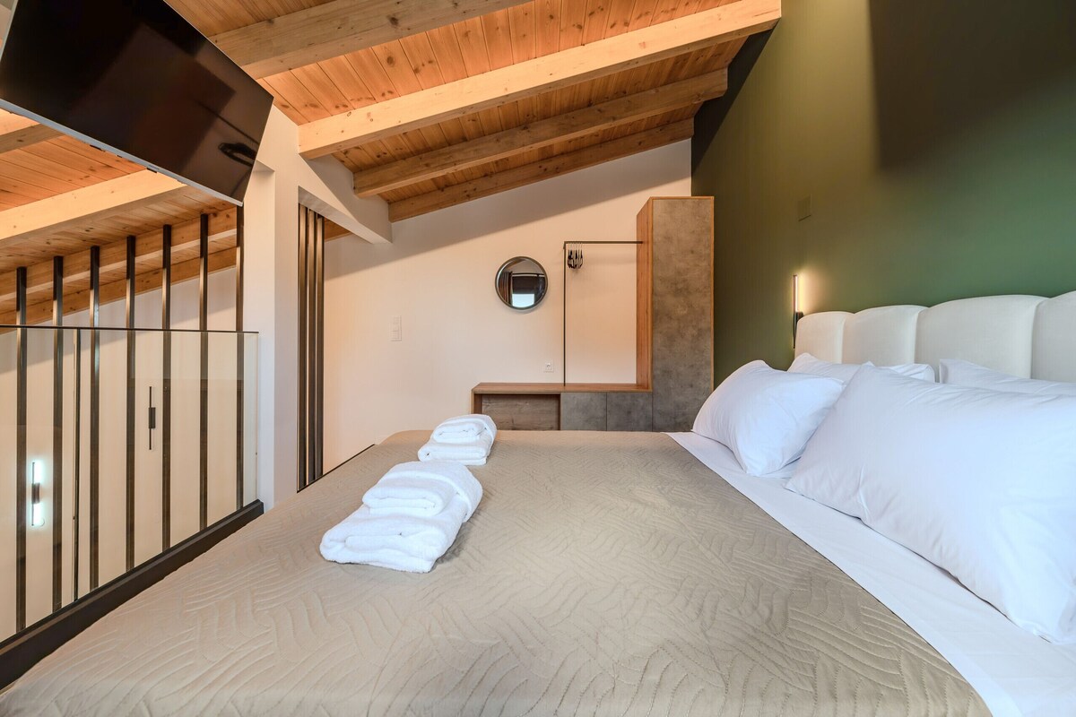 A modern hotel room with a large bed, a wooden ceiling, a round mirror, and a glass partition.