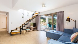 A modern living room with a wooden staircase, a blue sofa, and a TV on a wooden stand. - Sugar Premium Villa (Mylopotamos)