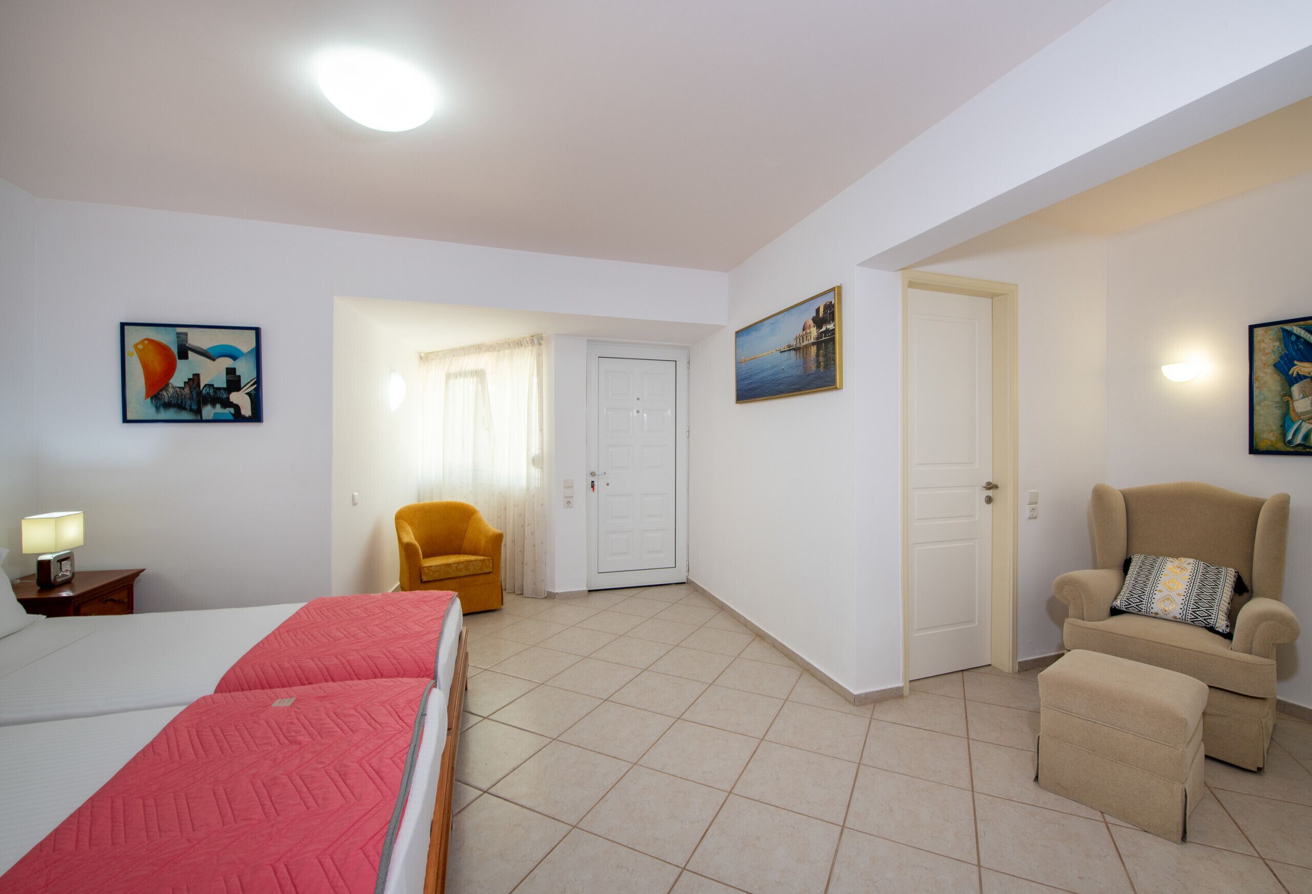 A hotel room with a bed, a chair, a sofa, and a door leading to another room.