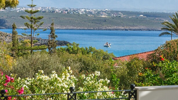 A coastal restaurant with outdoor seating overlooking a bay, a mountain in the background, and a clear sky. - Villa Plumeria Flower (Chania)