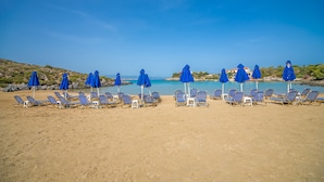 A beach with rows of blue umbrellas and lounge chairs. - Villa Plumeria Flower (Chania)