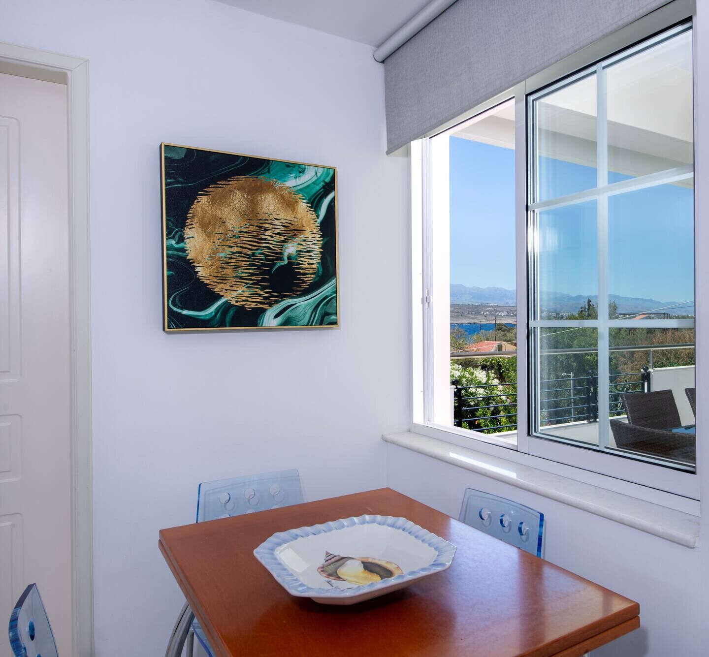 Una habitación con una mesa de comedor, una sola silla, una ventana con vistas a un paisaje y un cuadro en la pared.