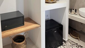 A modern bathroom with a black refrigerator, a wooden shelf, a woven basket, and a hanging wooden hanger. - Fira Basement Studios (Santorini)