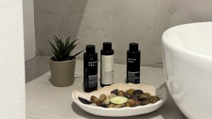 A bathroom with a white sink, a small potted plant, and three bottles of olive oil products. - Fira Basement Studios (Santorini)
