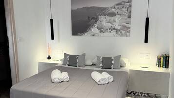 Cama arrumada com toalhas, fotografia costeira a preto e branco acima dela e azulejos de padrão no chão.