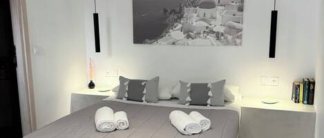 A neatly made bed with towels, a black and white coastal photograph above it, and patterned floor tiles.