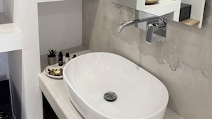 A modern bathroom with a white sink, a large mirror, and shelves with potted plants. - Fira Basement Studios (Santorini)