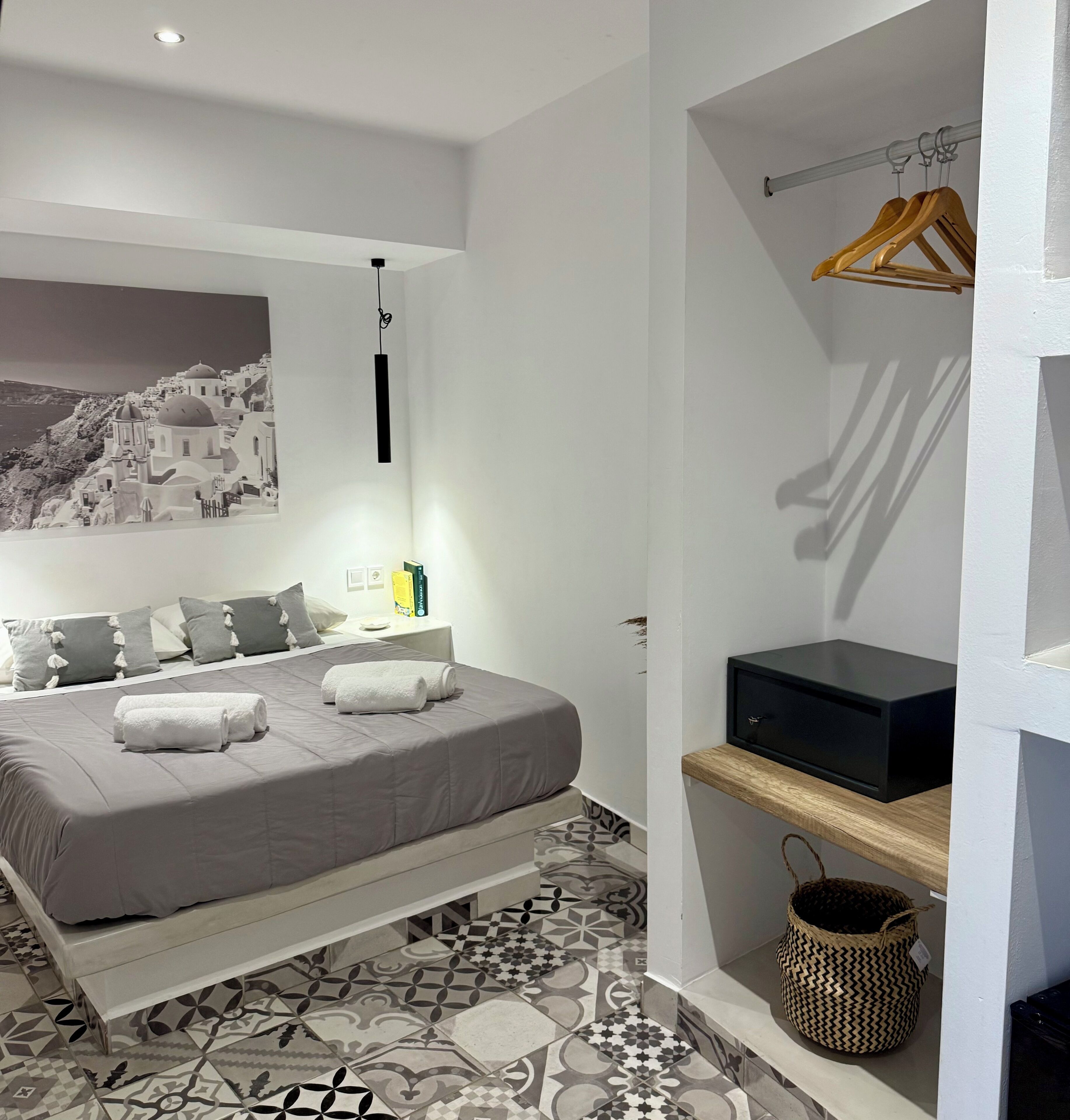 A bedroom with a bed, a wall-mounted TV, a shelf with a basket, and a hanging light fixture.