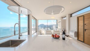 Una cocina moderna con una isla grande, vistas al mar y un comedor con mobiliario blanco.