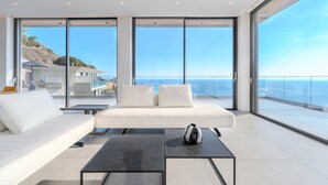 Una sala de estar moderna con un sofá blanco, dos mesas de centro negras y vista al océano.